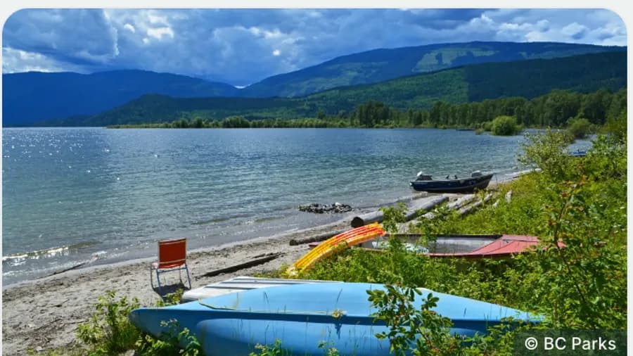 Canoes and kayaks pulled up on a lakeshore below forested hills