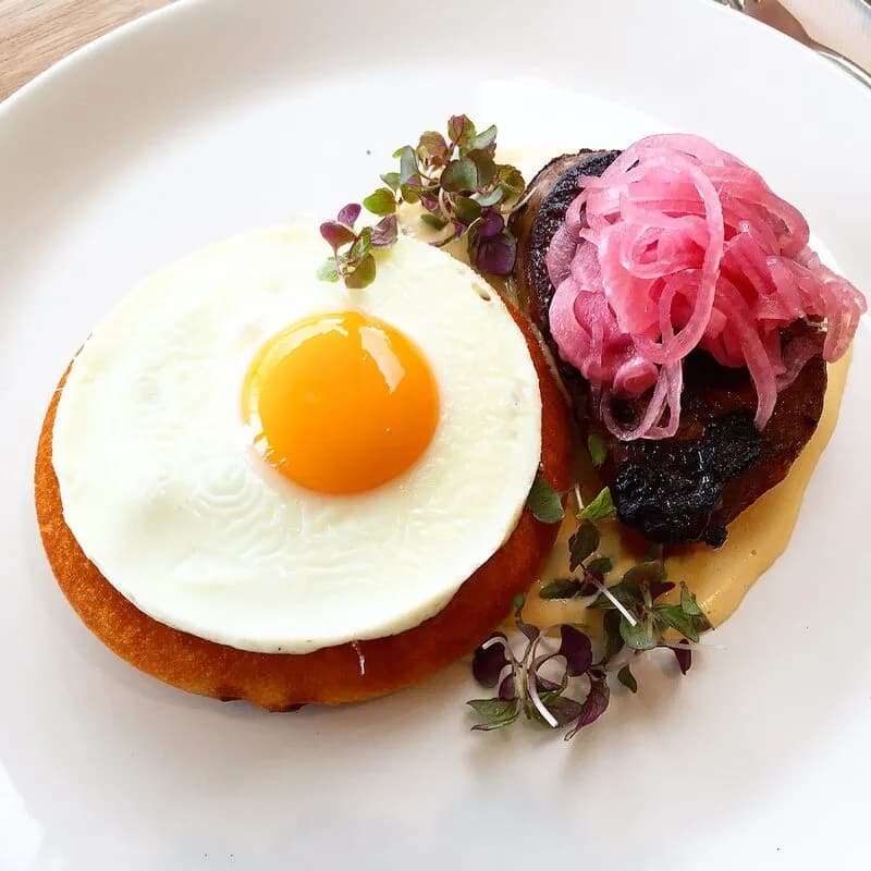 A fried egg on a crumpet beside seared pork belly with pickled red onion