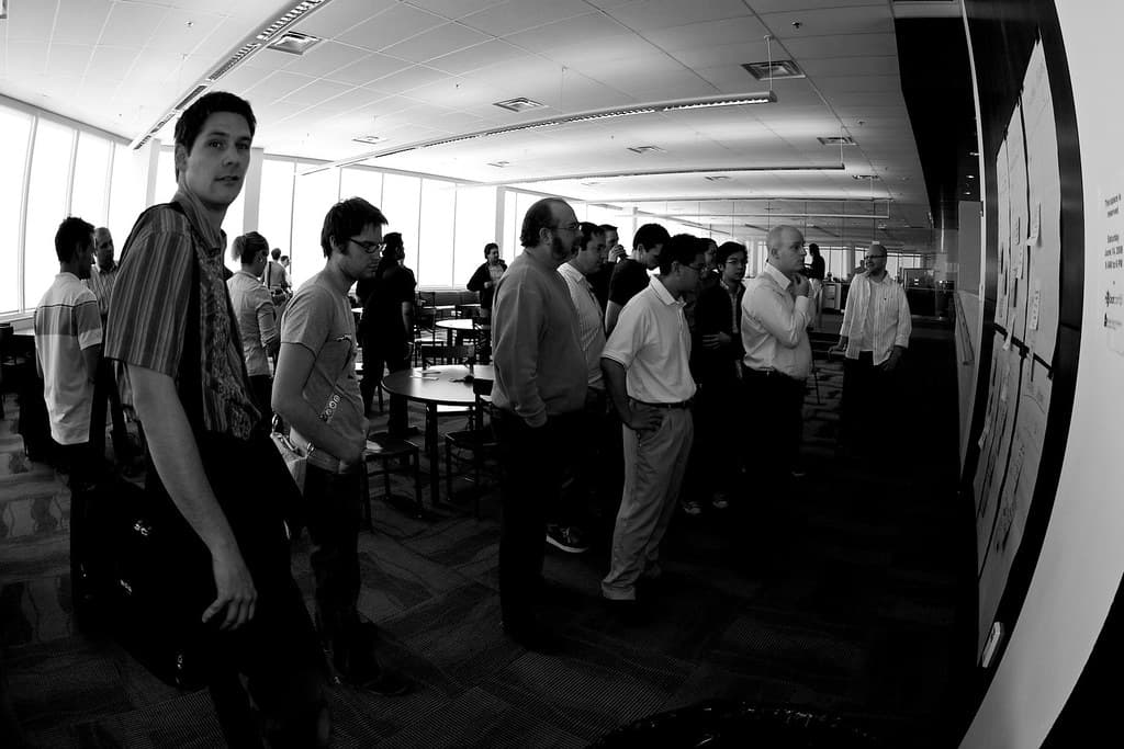 People reading the session sheets pinned along a wall at DemoCamp Calgary