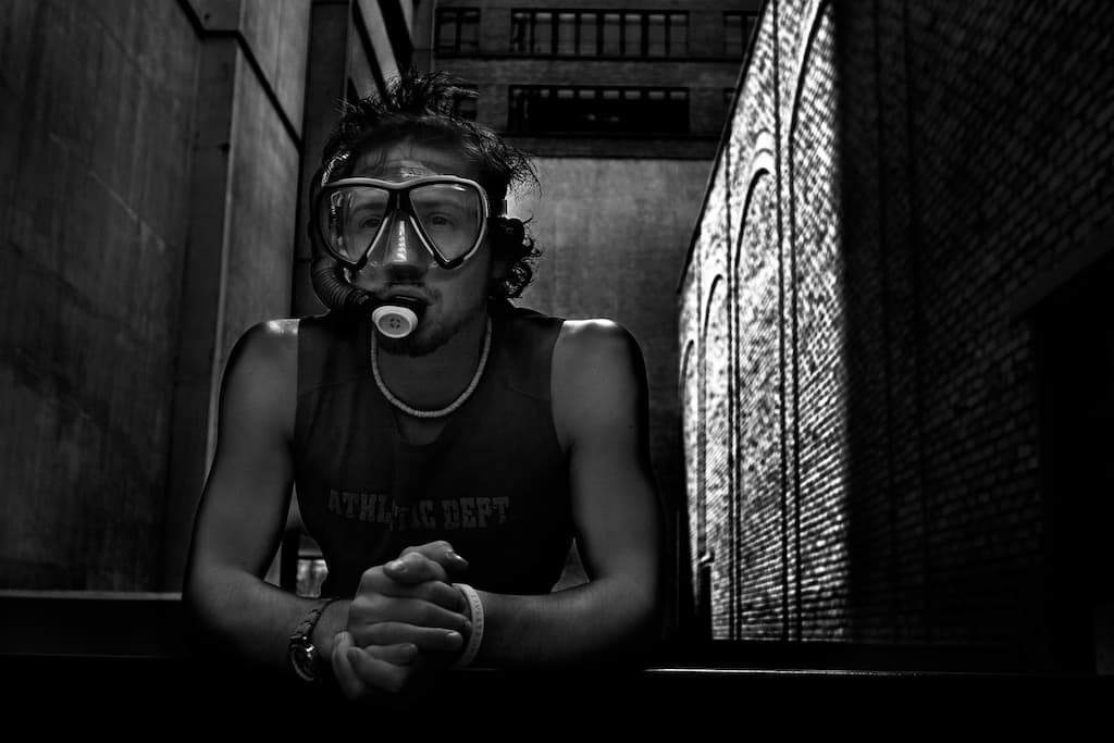A portrait in a dive mask and snorkel, leaning on a ledge between brick walls